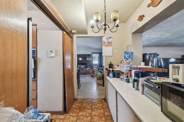 kitchen featuring light countertops, a textured ceiling, light floors, a fireplace, and a chandelier