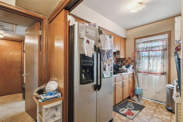 kitchen featuring light floors, light countertops, backsplash, brown cabinetry, and stainless steel fridge