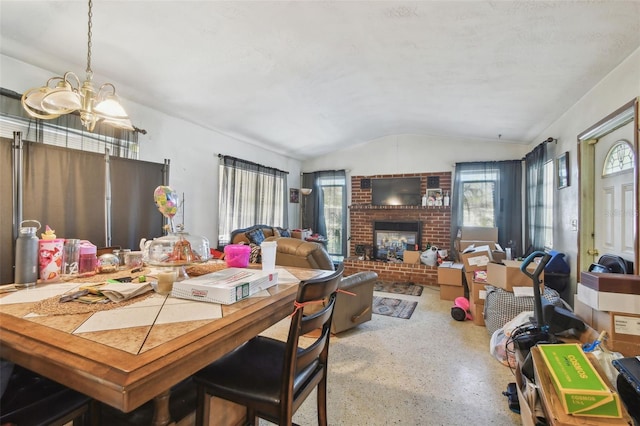 dining room with lofted ceiling, a brick fireplace, a notable chandelier, and plenty of natural light