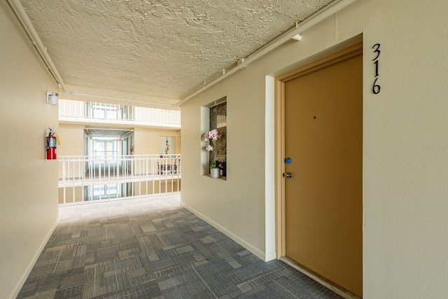 corridor with dark colored carpet, a textured ceiling, and baseboards