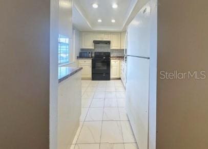 kitchen featuring a tray ceiling, light tile patterned floors, decorative backsplash, range, and under cabinet range hood