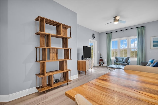 living area featuring baseboards, light wood-style floors, and a ceiling fan