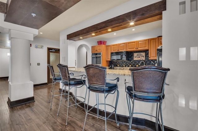 kitchen featuring backsplash, oven, black microwave, arched walkways, and dark wood-style flooring