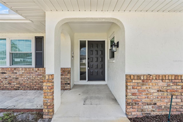 property entrance featuring covered porch, brick siding, and stucco siding