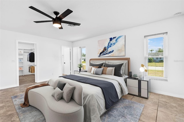 bedroom with light tile patterned floors, a walk in closet, a ceiling fan, and baseboards