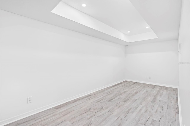 empty room with a tray ceiling, baseboards, light wood finished floors, and recessed lighting