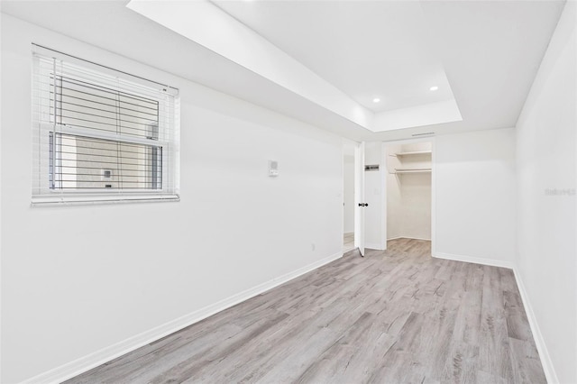 empty room with a raised ceiling, recessed lighting, wood finished floors, and baseboards