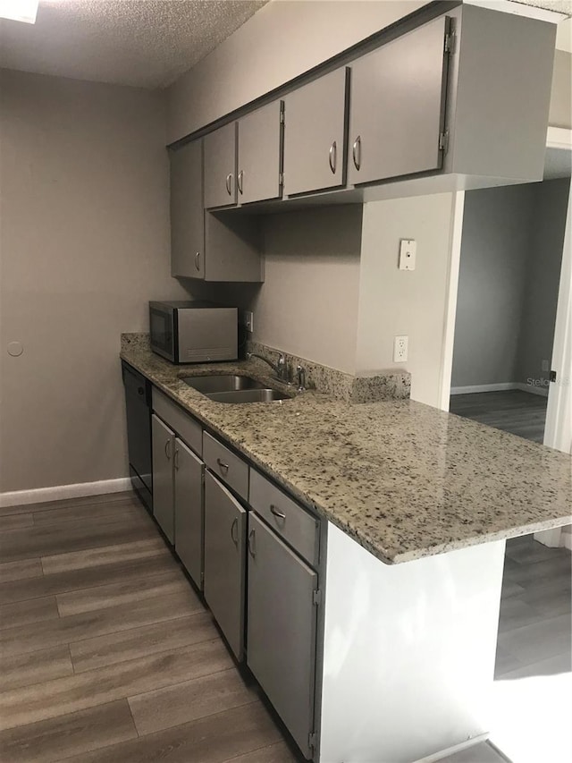 kitchen with stainless steel microwave, dark wood-type flooring, black dishwasher, a textured ceiling, and a sink