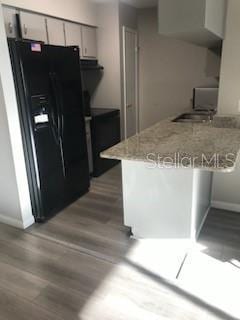 kitchen featuring baseboards, a peninsula, wood finished floors, and black refrigerator with ice dispenser