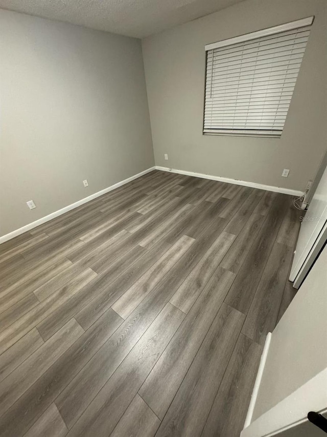 spare room featuring baseboards, dark wood-type flooring, and a textured ceiling