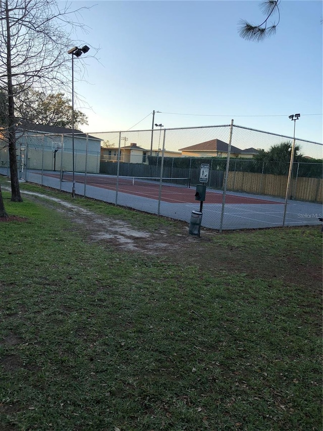 view of tennis court with a yard and fence