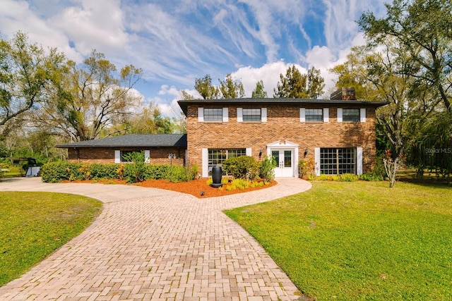 colonial house featuring decorative driveway, a front yard, french doors, and brick siding