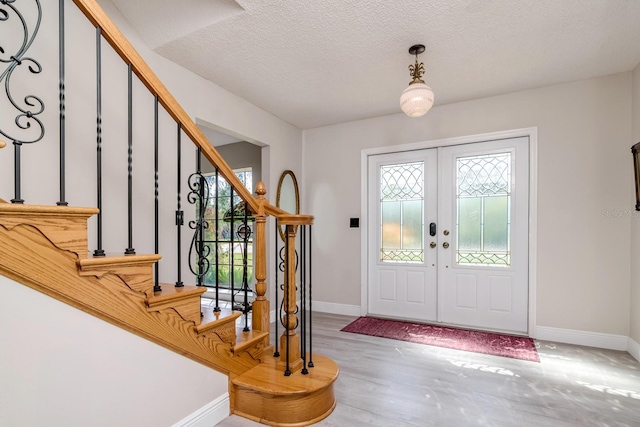 entrance foyer featuring french doors, a textured ceiling, wood finished floors, baseboards, and stairs