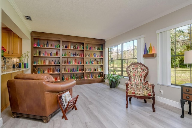 living area with light wood-style floors, a healthy amount of sunlight, visible vents, and a textured ceiling