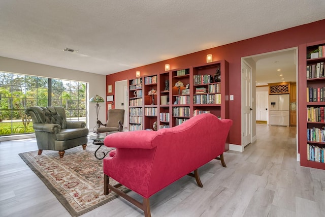 living area with a textured ceiling, baseboards, visible vents, and light wood-style floors