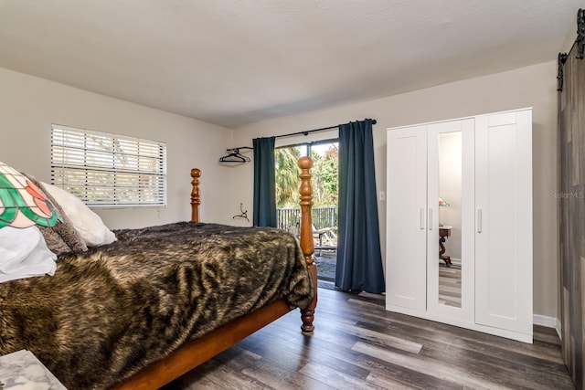 bedroom featuring dark wood-style floors, a barn door, and access to exterior