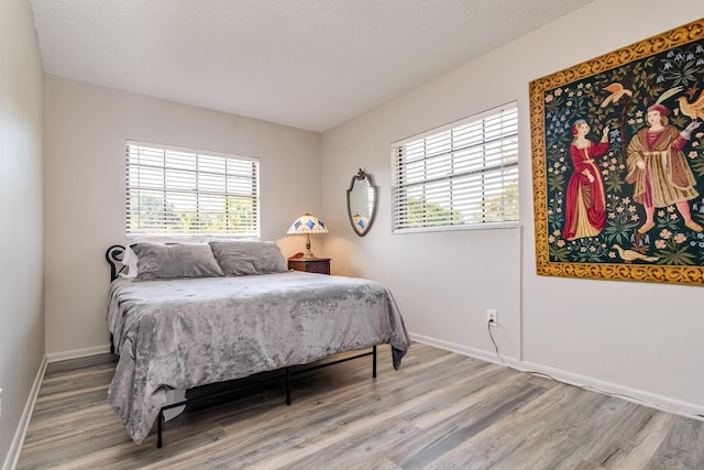 bedroom with multiple windows, wood finished floors, and baseboards