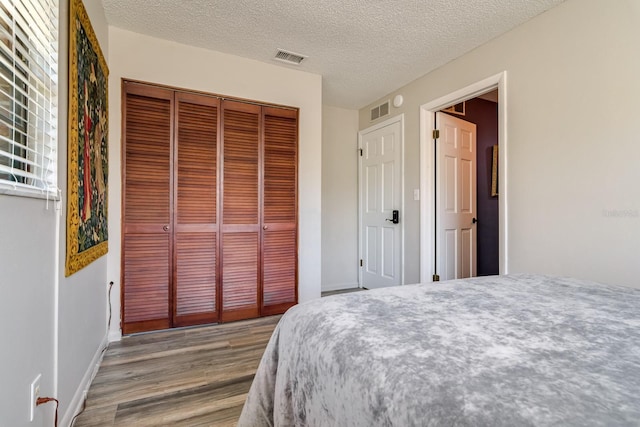 bedroom with a textured ceiling, a closet, wood finished floors, and visible vents