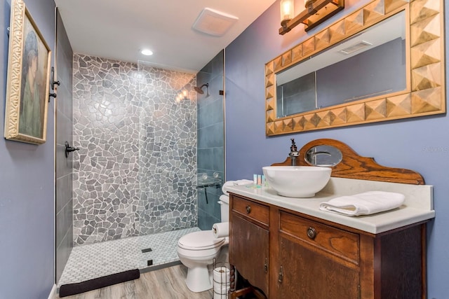full bath featuring tiled shower, vanity, toilet, and wood finished floors