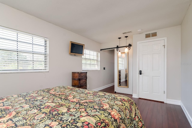 bedroom with dark wood-style floors, a barn door, visible vents, and baseboards