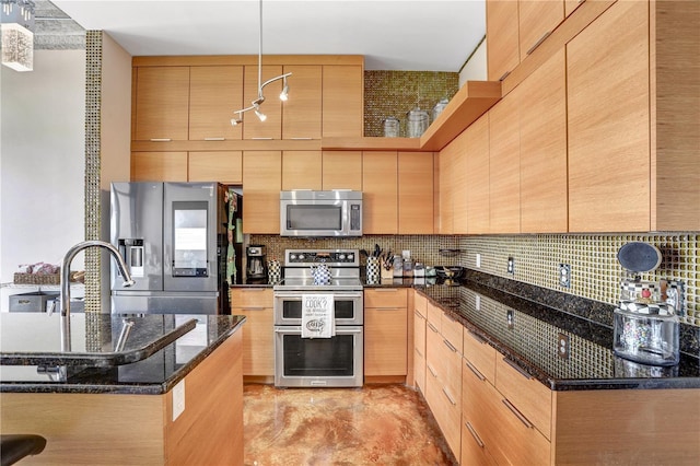 kitchen with light brown cabinets, appliances with stainless steel finishes, dark stone counters, and backsplash