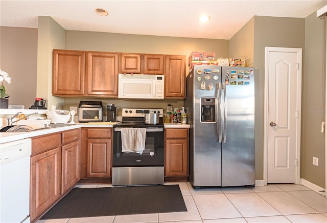 kitchen featuring light tile patterned floors, brown cabinetry, stainless steel appliances, light countertops, and a sink