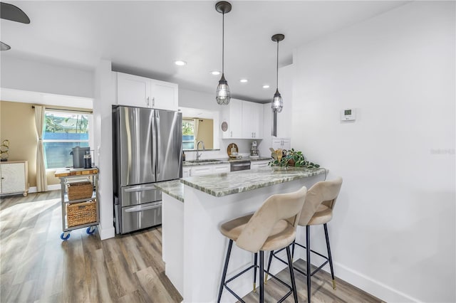 kitchen with light wood finished floors, appliances with stainless steel finishes, a breakfast bar area, a healthy amount of sunlight, and white cabinetry