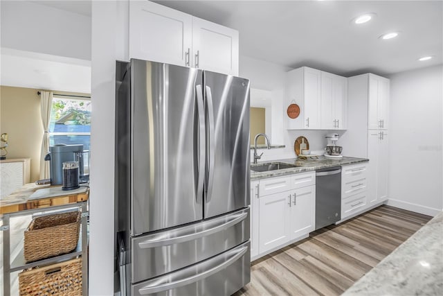 kitchen with stainless steel appliances, a sink, white cabinetry, light wood-type flooring, and light stone countertops