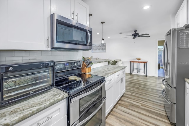 kitchen with light wood-style flooring, appliances with stainless steel finishes, light stone countertops, white cabinetry, and backsplash