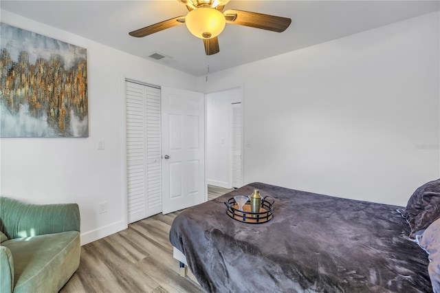 bedroom with wood finished floors, visible vents, baseboards, a ceiling fan, and a closet