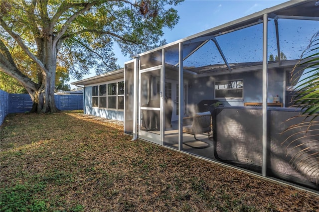 exterior space featuring glass enclosure, fence, and a lawn