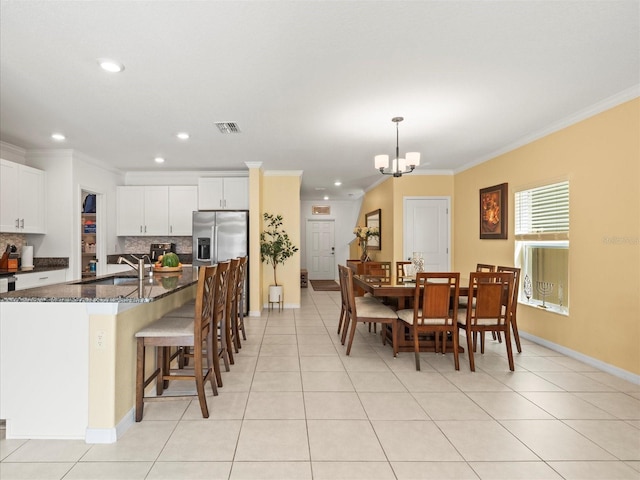 kitchen featuring light tile patterned floors, a sink, stainless steel refrigerator with ice dispenser, backsplash, and crown molding