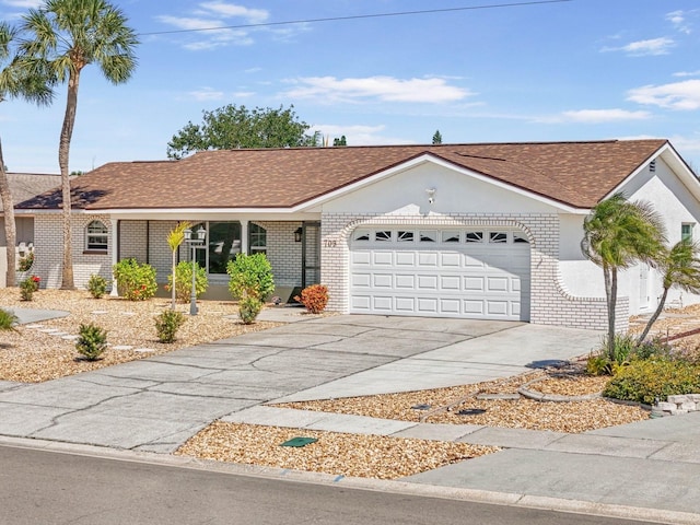 ranch-style home with brick siding, an attached garage, roof with shingles, and driveway