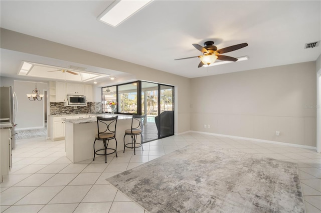 kitchen with stainless steel appliances, a kitchen bar, light tile patterned flooring, and ceiling fan with notable chandelier