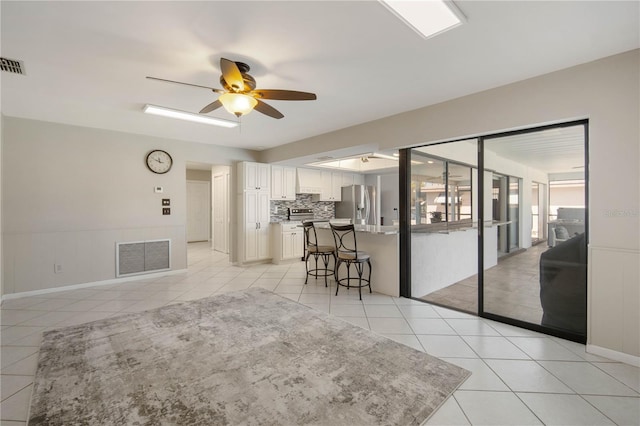 living room with light tile patterned floors, visible vents, a wainscoted wall, and a ceiling fan