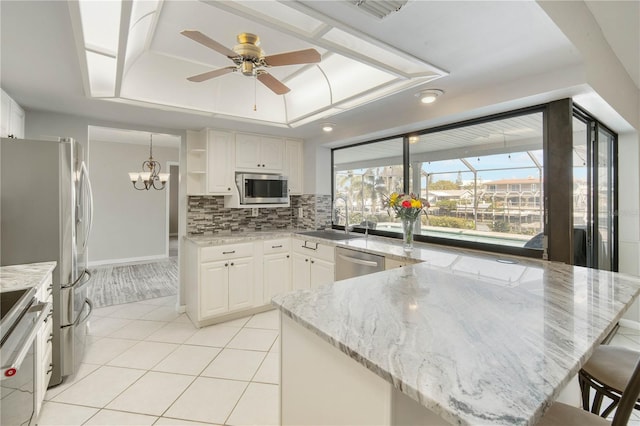 kitchen with a sink, appliances with stainless steel finishes, a peninsula, light tile patterned floors, and a raised ceiling