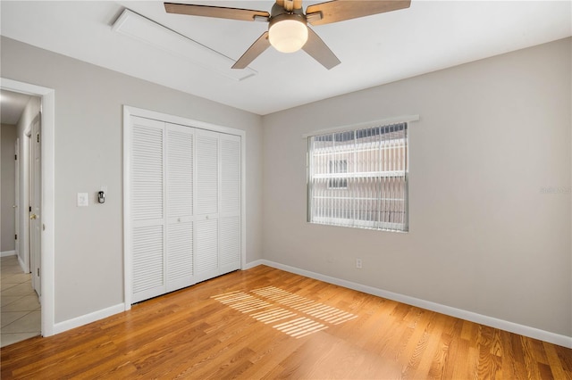 unfurnished bedroom with a ceiling fan, wood finished floors, a closet, baseboards, and attic access