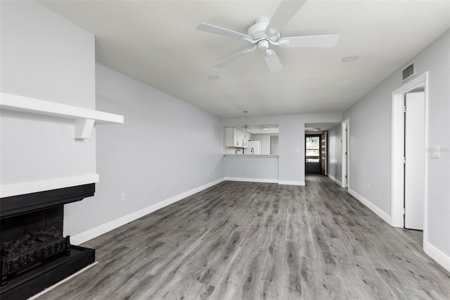 unfurnished living room featuring a fireplace with raised hearth, visible vents, ceiling fan, wood finished floors, and baseboards