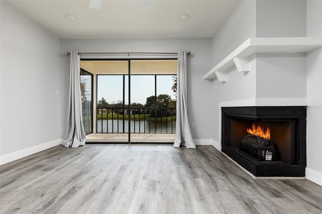 unfurnished living room with a warm lit fireplace, baseboards, and wood finished floors