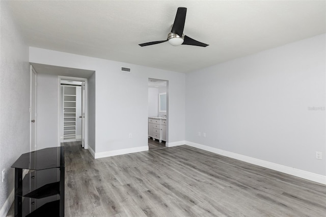 unfurnished bedroom featuring connected bathroom, wood finished floors, visible vents, baseboards, and a spacious closet