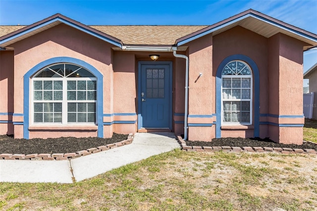 view of exterior entry featuring roof with shingles and stucco siding