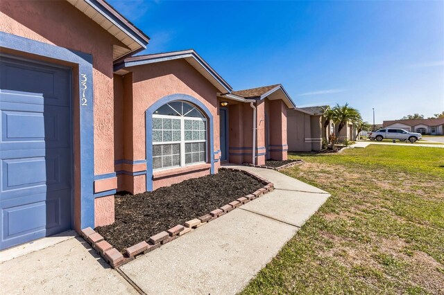 view of exterior entry featuring a garage, a lawn, and stucco siding