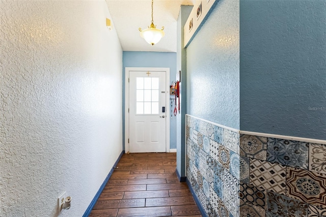 doorway featuring baseboards, dark wood-style flooring, and a textured wall