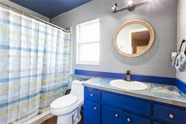 bathroom with a shower with shower curtain, toilet, a textured wall, wood finished floors, and vanity