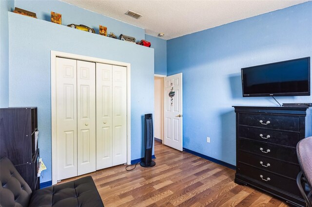 bedroom featuring baseboards, visible vents, wood finished floors, a textured ceiling, and a closet