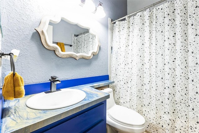 bathroom with toilet, vanity, a shower with shower curtain, and a textured wall