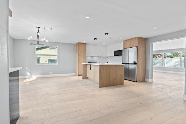 kitchen with light countertops, light wood-style flooring, freestanding refrigerator, modern cabinets, and black microwave