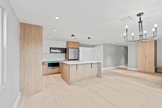 kitchen featuring modern cabinets, freestanding refrigerator, light countertops, light wood-style floors, and black microwave