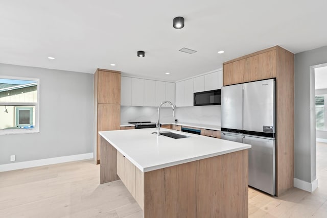 kitchen featuring modern cabinets, black microwave, a sink, and freestanding refrigerator