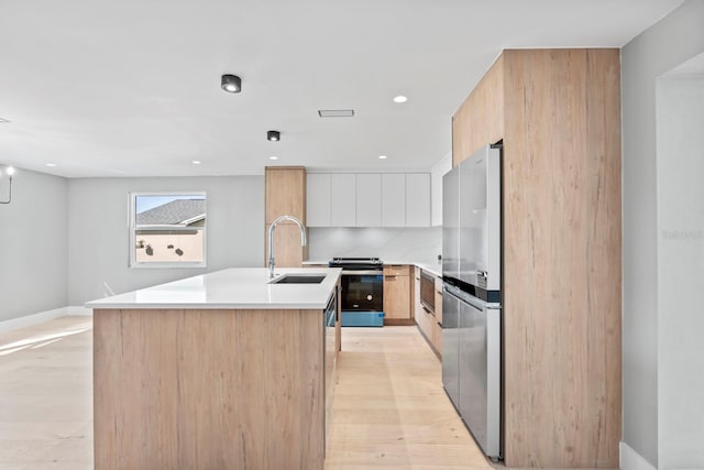 kitchen with a kitchen island with sink, a sink, light wood-style floors, appliances with stainless steel finishes, and modern cabinets